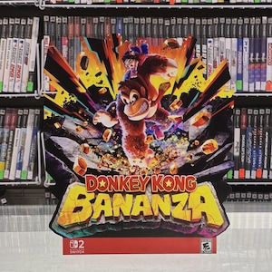 Puede incluir: Un colorido letrero promocional del juego para Nintendo Switch "Donkey Kong Bananza". La obra de arte presenta a Donkey Kong con un personaje montado en su espalda, sobre un fondo lleno de acción con el título del juego en letras amarillas grandes.