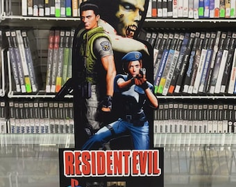 May include: A Resident Evil promotional display featuring game characters and the game's logo. The display is in front of shelves filled with video game cases. The PlayStation and Capcom logos are also visible.
