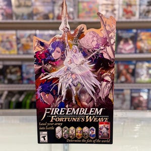 May include: A promotional cardboard display for the video game Fire Emblem Fortune's Weave, featuring multiple anime-style characters, a central winged figure, the game title, the text Lead your army into battle, and the ESRB Teen rating symbol.