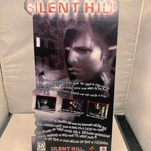 May include: A promotional poster for the video game "Silent Hill." The poster features the game's title in a glowing red font at the top. The image includes a grayscale portrait of a man and several smaller images from the game.