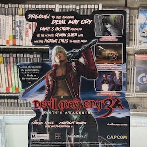 Könnte beinhalten: Werbeplakat für das Videospiel "Devil May Cry 3: Dante's Awakening" mit einer Figur mit weißen Haaren und einer roten Jacke, die ein Schwert hält. Das Plakat enthält Spieldetails und das PlayStation 2-Logo.