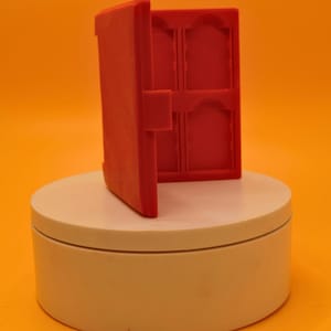 May include: A red, open, plastic card holder with four compartments. The holder is hinged and has a latch to close it. It is displayed on a white, circular platform against an orange background.