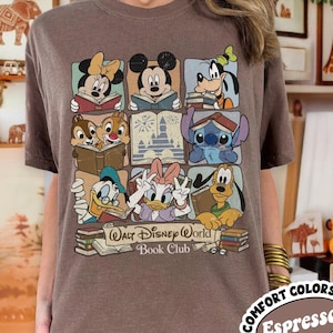 Puede incluir: Camiseta color espresso con un gr&aacute;fico de personajes de Disney leyendo libros. El dise&ntilde;o incluye a Minnie Mouse, Mickey Mouse, Goofy, Chip y Chop, Stitch, Donald Duck, Daisy Duck y Pluto. Tambi&eacute;n est&aacute; presente el texto "Walt Disney World Book Club".