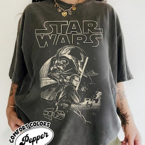 May include: Dark grey t-shirt with a Star Wars graphic featuring Darth Vader and Luke Skywalker. The text "STAR WARS" is printed across the top. The shirt has a vintage, distressed appearance and the Comfort Colors Pepper logo.