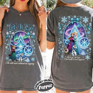 Puede incluir: Camiseta gris carb&oacute;n con un gr&aacute;fico colorido de la pel&iacute;cula Frozen. El dise&ntilde;o frontal incluye el texto "Let It Go" y la frase "The cold never bothered me anyway." El dise&ntilde;o trasero muestra a Elsa y Anna con el texto "Let it go, let it go... Can't hold it back anymore."