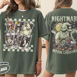 May include: Moss green t-shirt featuring graphics from "The Nightmare Before Christmas." The front displays character cards, while the back showcases Oogie Boogie and other characters with the text "Nightmare Before Christmas."