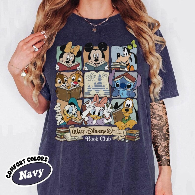 Puede incluir: Camiseta azul marino con un dise&ntilde;o de cuadr&iacute;cula de personajes de Disney leyendo libros, incluyendo Mickey y Minnie Mouse. La camiseta tiene el texto "Walt Disney World Book Club" y "Comfort Colors" impresos.