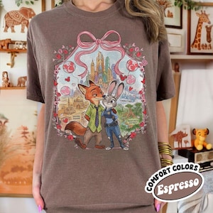 May include: Espresso-colored t-shirt featuring a graphic of Nick Wilde and Judy Hopps from Zootopia. The design includes a pink bow, hearts, and cityscapes. The shirt has a crew neck and short sleeves. The words "COMFORT COLORS" and "Espresso" are printed on the bottom right.