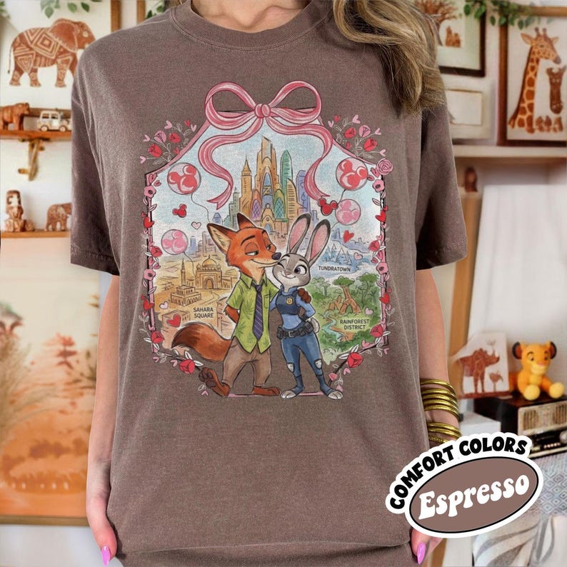 May include: Espresso-colored t-shirt featuring a graphic of Nick Wilde and Judy Hopps from Zootopia. The design includes a pink bow, hearts, and cityscapes. The shirt has a crew neck and short sleeves. The words "COMFORT COLORS" and "Espresso" are printed on the bottom right.