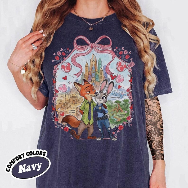 May include: Navy blue t-shirt featuring a colorful illustration of Nick Wilde and Judy Hopps from Zootopia. The design includes a cityscape, hearts, and the words "Sahara Square", "Tundratown", and "Rainforest District". The shirt has the words "Comfort Colors" and "Navy".