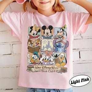 Puede incluir: Camiseta rosa claro con un gr&aacute;fico colorido de personajes de Disney leyendo libros. El dise&ntilde;o incluye Mickey Mouse, Minnie Mouse, Goofy, Pato Donald, Daisy, Chip y Chop, Stitch y Pluto. Tambi&eacute;n se incluye el texto "Walt Disney World Book Club".