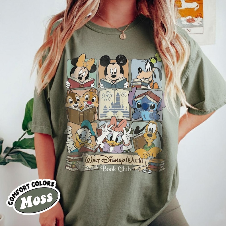 Puede incluir: Camiseta verde musgo con un gr&aacute;fico colorido de personajes de Disney leyendo libros. El dise&ntilde;o incluye Mickey Mouse, Minnie Mouse, Goofy, Pato Donald, Daisy, Chip y Chop y Stitch. El texto "Walt Disney World Book Club" tambi&eacute;n est&aacute; impreso.