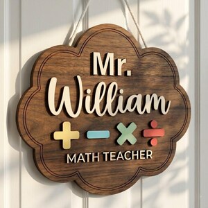 May include: A wooden sign in a cloud shape, with the name "Mr. William" in white. Below are colourful math symbols and the words "MATH TEACHER". The sign is suspended by a natural rope, suitable for a classroom.