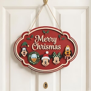 Pode incluir: Uma placa de parede oval de madeira vermelha com um cordão de juta para pendurar. O texto Merry Chrismas está centralizado em letras creme. Abaixo, cinco rostos de personagens de desenhos animados estão dispostos: Pateta, Pato Donald, Mickey, Minnie e Pluto.