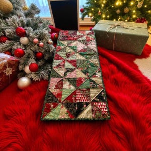 May include: A festive Christmas table runner with a patchwork design in red, green, and black. The runner sits on a red faux fur rug, with a decorated Christmas tree and wrapped gifts visible in the background.