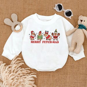 May include: White long-sleeve baby onesie with a Christmas-themed graphic of four capybaras wearing Santa hats, reindeer antlers, and a Christmas tree. The text "Merry Fetch-Mas" is printed below the capybaras.