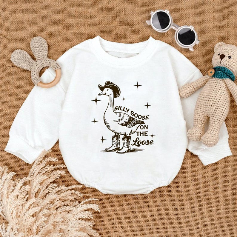 May include: White long-sleeve baby onesie with a black and white illustration of a goose wearing a cowboy hat and boots. The text "Silly Goose on the Loose" is printed below the goose.