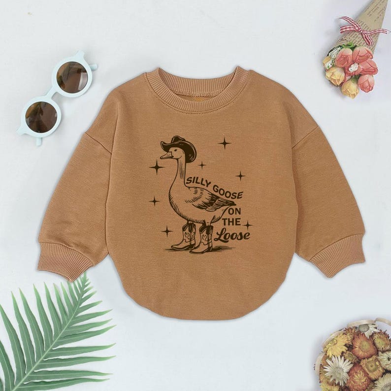May include: A brown long-sleeved sweatshirt with a graphic of a goose wearing a cowboy hat and boots. The text "Silly Goose on the Loose" is printed on the sweatshirt.