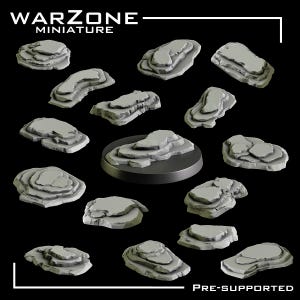 May include: A collection of grey, unpainted resin rock formations for miniature gaming bases, featuring various jagged, layered stone shapes. One rock is mounted on a circular black base. The text WARZONE MINIATURE and PRE-SUPPORTED is visible.