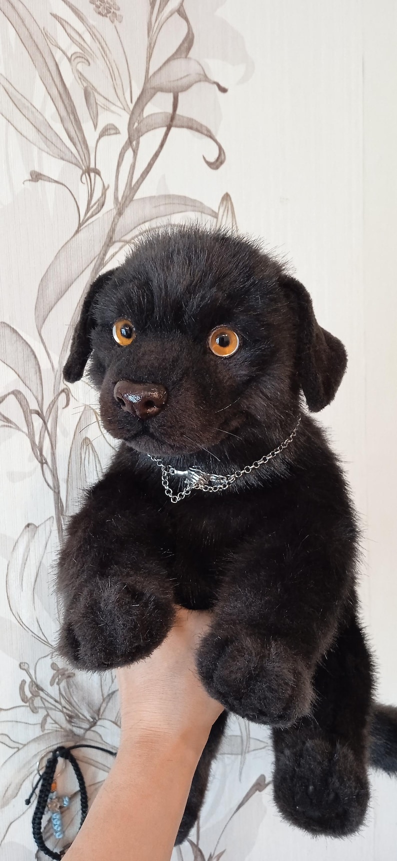 May include: A black plush puppy with amber eyes and a silver chain collar. The soft toy has a furry texture and a realistic appearance, with a detailed nose and ears. The puppy is a charming, handcrafted item.