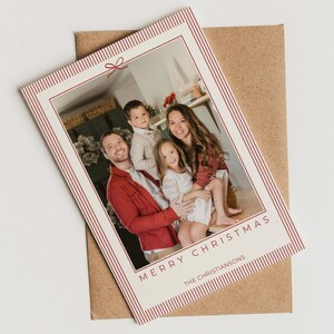May include: A Christmas card featuring a family portrait, with the words "MERRY CHRISTMAS" and "THE CHRISTIANSONS" printed in red. The card has a red and white striped border and is placed on a brown envelope.