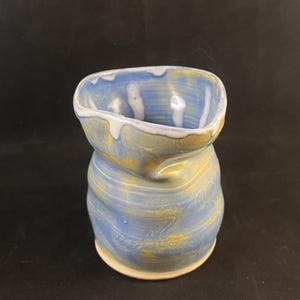 May include: A blue and gold ceramic vase with a unique, wavy design. The vase has a wide opening and a narrow base.