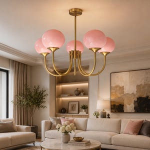 May include: A multi-arm chandelier featuring a central brass-toned metal rod and curved arms that support five spherical, light pink glass globes. The fixture is suspended from the ceiling by a matching circular brass-toned canopy mount.