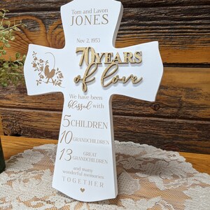 Pu&ograve; includere: Croce di legno bianco con il testo "Tom and Lavon JONES Nov 2, 1953 70 YEARS of love We have been blessed with 5 CHILDREN 10 GRANDCHILDREN 13 GREAT GRANDCHILDREN and many wonderful memories TOGETHER" in lettere dorate.