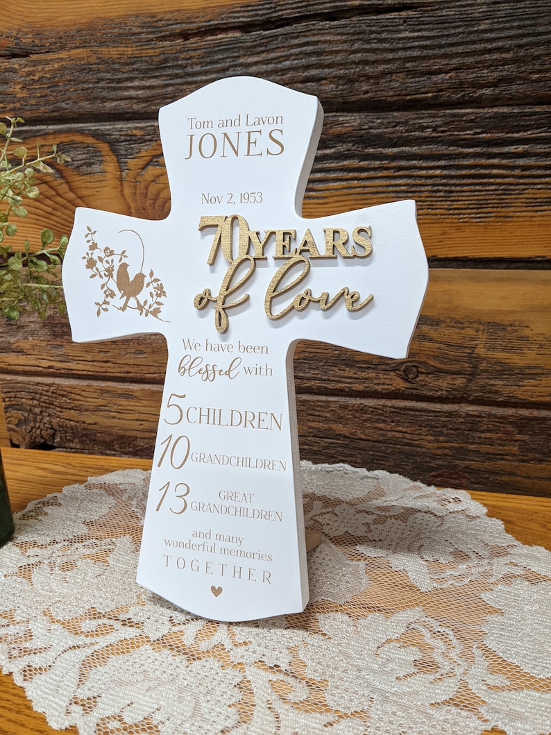 Pu&ograve; includere: Croce di legno bianco con il testo "Tom and Lavon JONES Nov 2, 1953 70 YEARS of love We have been blessed with 5 CHILDREN 10 GRANDCHILDREN 13 GREAT GRANDCHILDREN and many wonderful memories TOGETHER" in lettere dorate.
