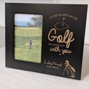 May include: Black picture frame with a gold inscription that reads "I'd give my best day to Golf one more day with you" with a heart symbol and a golf bag illustration. The inscription is in memory of Uncle Johnny. The frame has a photo of a golfer on a green.