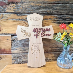 Op de afbeelding: Een houten kruis met de tekst "Daniel & Donna MANGIN August 28, 1982" en "40 YEARS of love" erop gegraveerd. Het kruis heeft ook een klein vogeltje en een bloemmotief. De tekst "I have found the one whom my soul loves." is gegraveerd op de onderkant van het kruis.