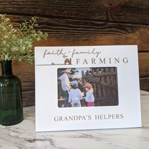 May include: White picture frame with the text "faith family farming grandpa's helpers" and a photo of a man and two children in front of a wooden fence.