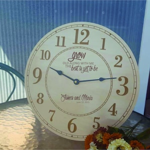 May include: A wooden clock with a light brown face and black hands. The clock has Roman numerals and the text "grow old along with me the best is yet to be". The clock is personalized with the names "James and Maria" and the date "June 12, 2015".