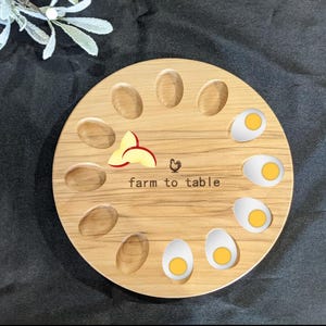 May include: A wooden egg holder with 12 slots, featuring a chicken silhouette and the text "farm to table". The holder is filled with eggs, some with visible yolks.