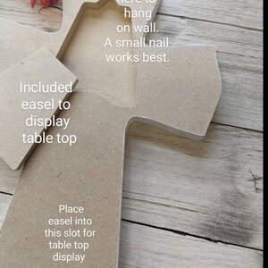 Pu&ograve; includere: Una croce di legno con una tacca per appenderla al muro. La croce ha una fessura per un cavalletto per esporla su un tavolo. Il testo "Use notch here to hang on wall. A small nail works best." e "Included easel to display table top" e "Place easel into this slot for table top display" &egrave; stampato sulla croce.