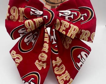 May include: Red and gold bow with the San Francisco 49ers logo repeated on the fabric.