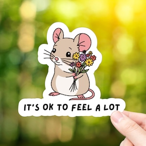 May include: A sticker featuring a cartoon mouse holding a bouquet of colorful flowers. The text "It's ok to feel a lot" is written below the mouse.