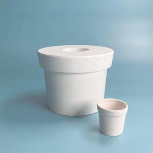 Może przedstawiać: Dwa białe ceramiczne doniczki, jedna duża i jedna mała, na jasnoniebieskim tle. Większa doniczka ma szeroki, okrągły otwór na górze.