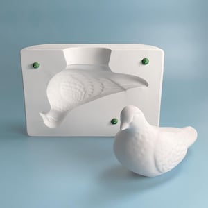 Op de afbeelding: Een witte keramische mal voor het maken van een duivenbeeldje. De mal wordt getoond met een afgewerkt duivenbeeldje.