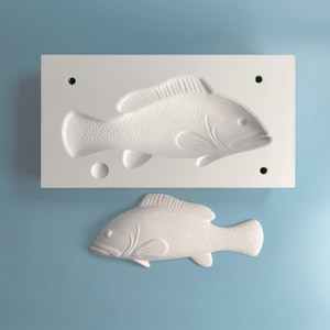 Puede incluir: Molde de silicona blanco para hacer pasteles u otras golosinas con forma de pez. El molde presenta dos diseños de peces, uno más grande que el otro.