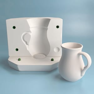 May include: White ceramic mold for making a pitcher, with a white ceramic pitcher next to it.