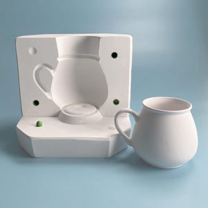 Pode incluir: Um molde de cerâmica branca para fazer um jarro ou um vaso, e uma caneca de cerâmica branca de forma arredondada com alça.