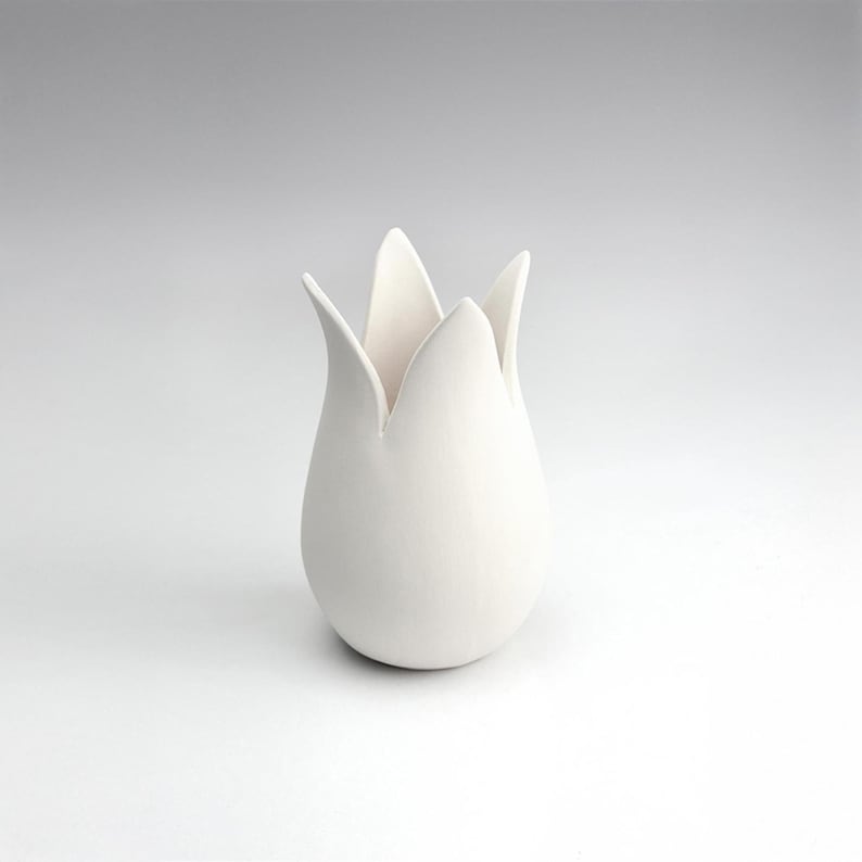 May include: A white ceramic vase shaped like a tulip with a wide opening at the top.