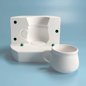 Può includere: Uno stampo in ceramica bianca per realizzare una tazza, con un pomello in plastica verde su ogni lato. Una tazza in ceramica bianca è posta accanto allo stampo.
