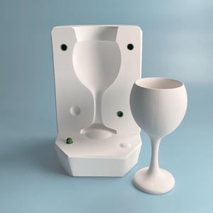 Può includere: Uno stampo bianco per realizzare un bicchiere da vino, con un bicchiere da vino bianco accanto.