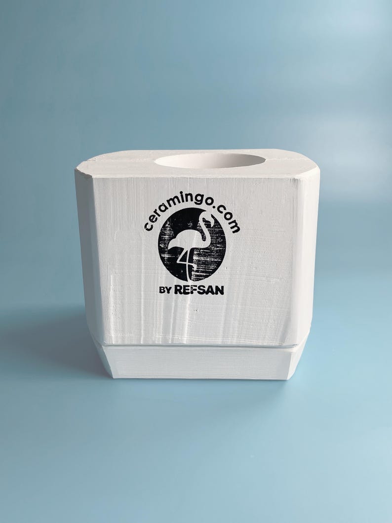 Pode incluir: Molde de cer&acirc;mica branco com uma abertura redonda no topo. O molde tem um logotipo que diz "ceramingo.com" com um gr&aacute;fico de flamingo e o texto "BY REFSAN" abaixo.