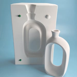 以下が含まれることがあります： ユニークでモダンなデザインのフラワーベースを作るための白いセラミックモールド。モールドは片側が開いており、滑らかでマットな仕上がりです。