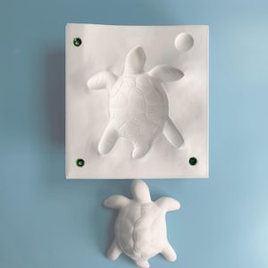 Puede incluir: Molde de yeso blanco de una tortuga, con una tortuga más pequeña hecha del mismo material debajo.