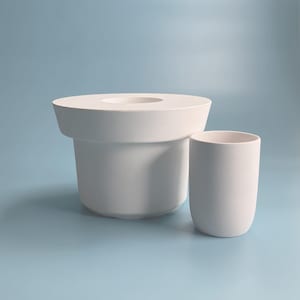 Peut inclure: Deux contenants en céramique blanche, l'un haut et cylindrique avec un bord large, l'autre plus court et cylindrique. Les deux sont sur un fond bleu clair.