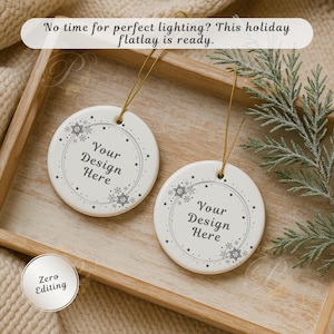 May include: Two white ceramic Christmas ornaments with gold hanging strings. Each ornament has a snowflake and star design around the edge, with the text "Your Design Here" in the center. The ornaments are in a wooden tray.